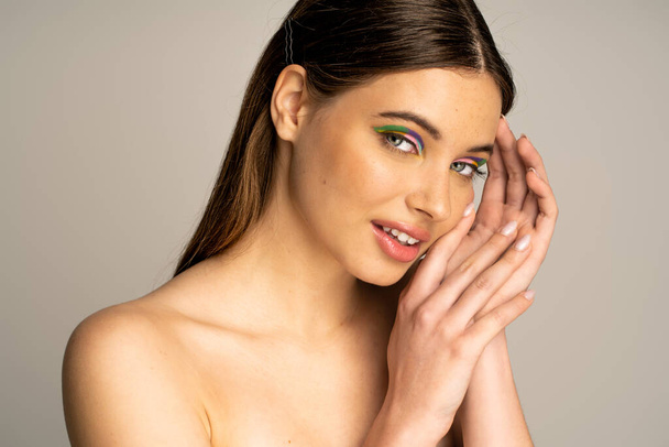 Smiling teen model with colorful makeup posing and looking at camera isolated on grey  - Photo, Image