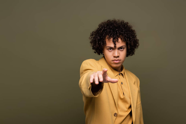 fiatal és göndör afro-amerikai férfi sárga kabátban, ujjal mutogatva a szürke kamerára. - Fotó, kép