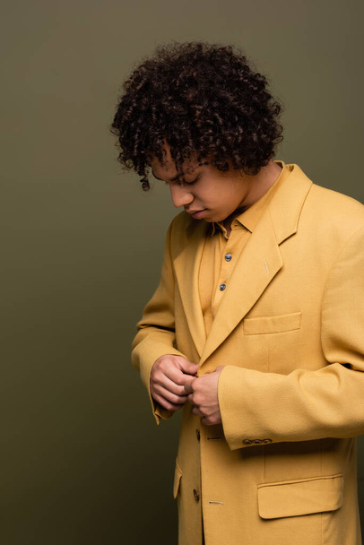 brunette african american man buttoning yellow blazer on olive grey background - Foto, Imagem