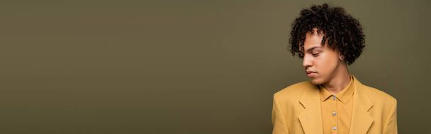 jong Afrikaans amerikaans guy met golvend brunette haar poseren in geel jas geïsoleerd op grijs, banner - Foto, afbeelding