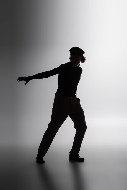 silhouette sombre de jeune homme afro-américain debout avec la main tendue sur fond gris - Photo, image