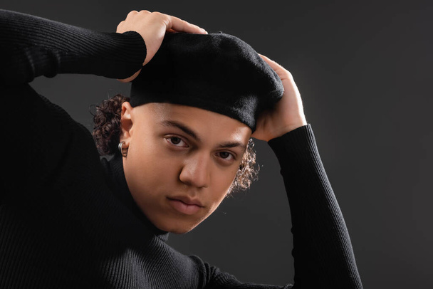 young and trendy african american man in black turtleneck adjusting beret and looking at camera isolated on dark grey - 写真・画像