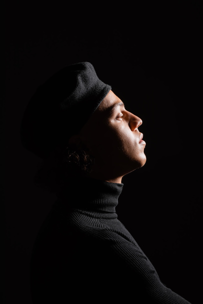 side view of fashionable african american man in turtleneck and sweater isolated on black - Photo, Image