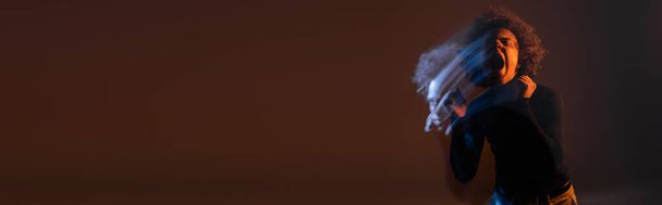 dubbele blootstelling van gewonde en boze Afro-Amerikaanse man schreeuwen op donkere achtergrond met rood en blauw licht, banner - Foto, afbeelding