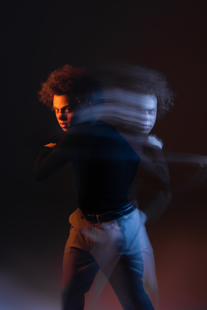 larga exposición de hombre afroamericano joven y herido con trastorno bipolar mirando a la cámara en negro con luz naranja y azul - Foto, Imagen