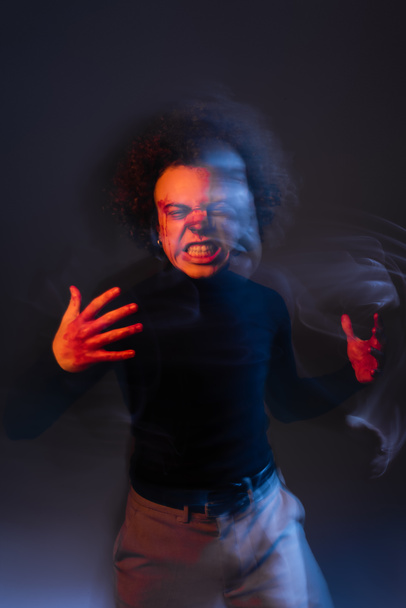 dvojité vystavení rozzlobený africký Američan muž se zraněnou tváří a bipolární poruchou šklebí na tmavé s oranžovým a modrým světlem - Fotografie, Obrázek