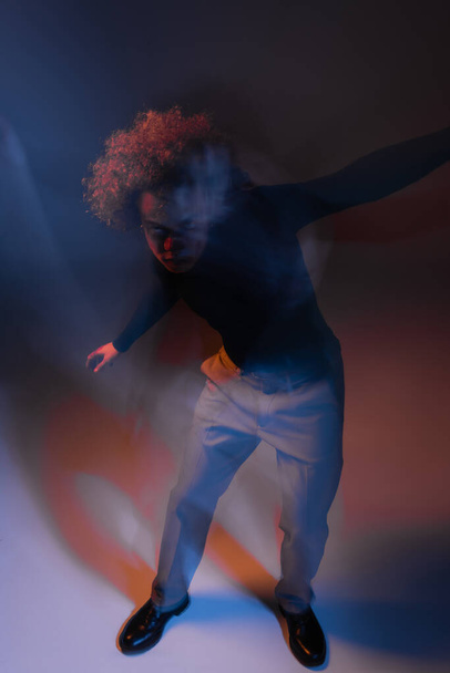 motion blur of abused and wounded african american man bipolar disorder looking at camera on dark with orange and blue light - Foto, Imagen