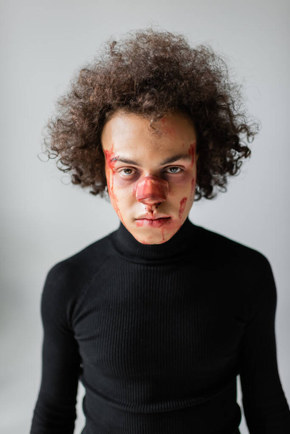 ranny Afroamerykanin ze złamanym nosem i krwawiącą twarzą patrzący na kamerę odizolowaną na szaro - Zdjęcie, obraz
