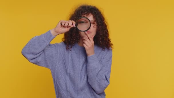 Onderzoeker onderzoeker wetenschapper vrouw houden vergrootglas in de buurt van gezicht, kijken in de camera met grote zoomde grappige ogen, zoeken, analyseren. jong krullend harig meisje op gele studio achtergrond - Video