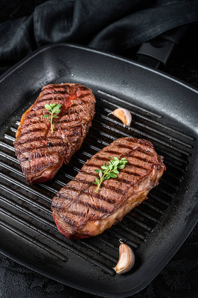 Grilled Top Blade or flat iron roast beef meat steaks on a skillet. Black background. Top View. - Zdjęcie, obraz