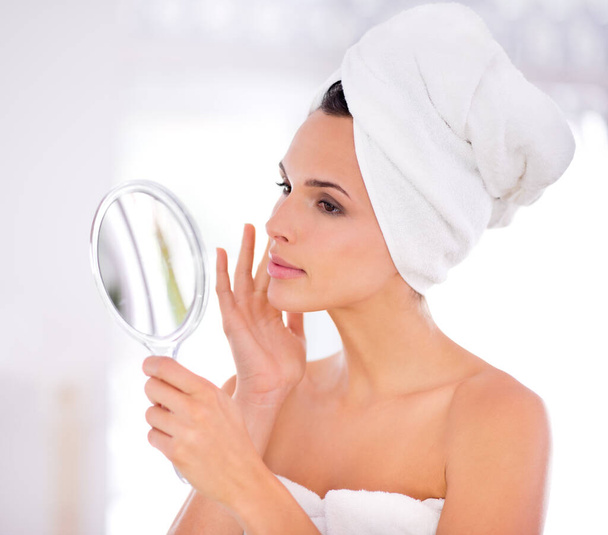 Μια όμορφη γυναίκα να χαϊδεύει το δέρμα της κρατώντας έναν καθρέφτη. - Φωτογραφία, εικόνα