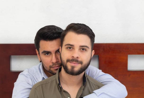 portrait of gay couple sitting on bed looking at camera - Zdjęcie, obraz
