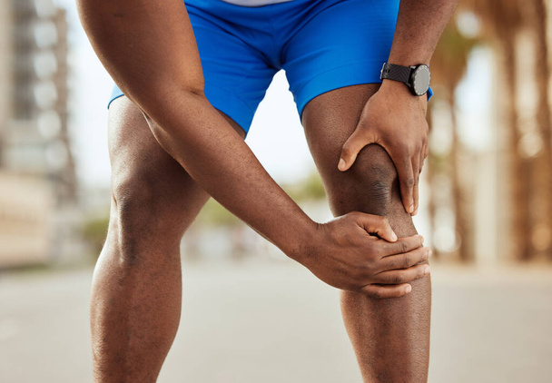 Fitness, pain in knee and hands of black man with muscle ache, joint pain and injury after running in city. Sports, body wellness and male athlete rest after workout, marathon training and exercise. - Foto, Bild