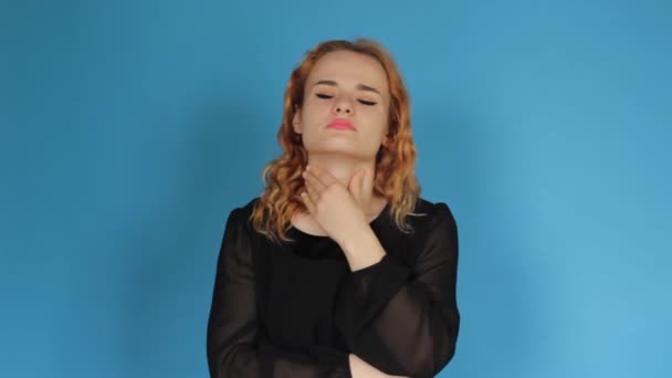 An unhealthy young woman touches her neck, it is difficult to swallow, experiencing discomfort or a painful feeling, isolated on a blue background studio - Filmagem, Vídeo