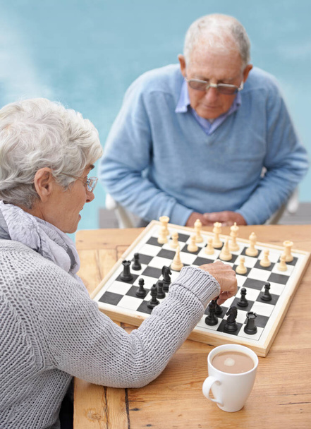 There..my knight takes your bishop. An elderly couple playing chess together on the patio - Foto, Bild