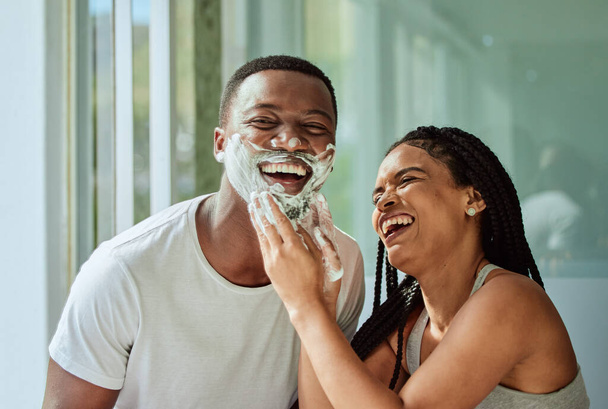 Skincare wellness, happy couple in bathroom and shaving face with product for facial treatment. Laughing together in home, natural beauty and funny girlfriend helping black man with cream application. - Fotó, kép
