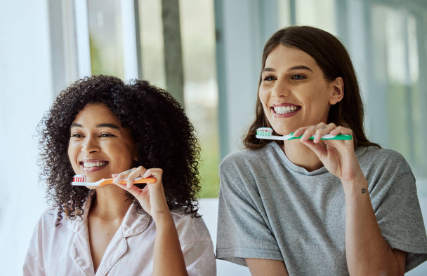 Toothbrush, oral care and women friends doing a dental, health and wellness morning routine together. Happy, smile and interracial females brushing their teeth for mouth hygiene in the bathroom - Photo, Image