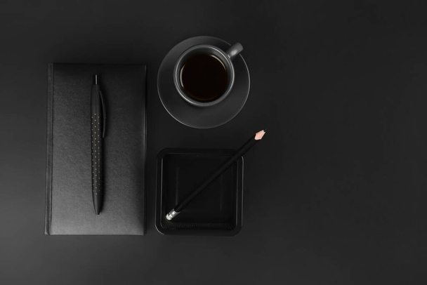Notebook with pen, pencil holder and cup of coffee on black background - Foto, Imagen