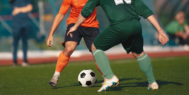 2人の大人のサッカー選手が決闘でサッカーボールを蹴る。2つのチームのサッカー大会。匿名の選手がボールを走ったり蹴ったり - 写真・画像