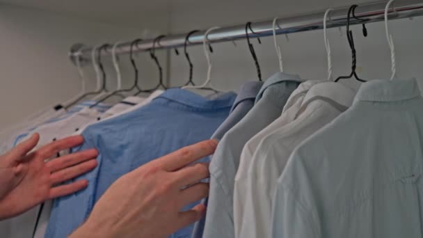 парень выбирает вешалки с другой рубашкой в гардеробе - Кадры, видео