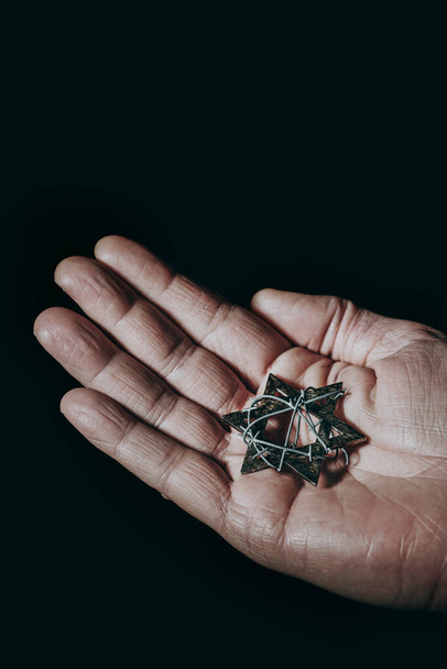 the hand of a man with a star of david tied with some barbed wire, against a black background - Photo, image