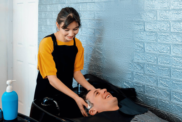 Caucasian man getting hair wash by professional hairdresser with shampoo feels relax and comfortable . Qualified hairdresser with her barbershop, salon providing haircare concept. - Photo, Image