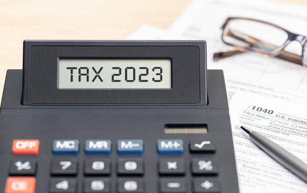 Tax time 2023 concept. Text on calculator screen and tax form on table - Photo, Image