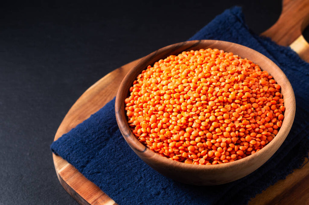 Healthy food concept red lentils in wooden bowl on black background with copy space - Foto, immagini