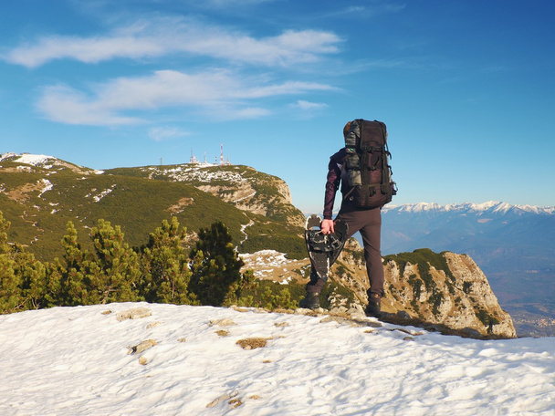 Турист с большим рюкзаком и снегоступами, стоящий на скалистой точке обзора и смотрящий в туманные скалистые горы. Национальный парк Альпы в Италии. Солнечное зимнее утро
. - Фото, изображение