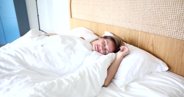 Attractive young woman wakes up in morning in bed. Comfortable healthy sleep - Materiał filmowy, wideo
