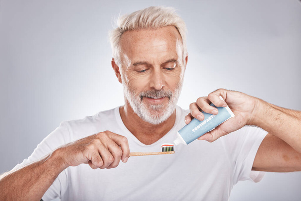 Face, toothpaste and senior man with toothbrush in studio isolated on a gray background. Hygiene, cleaning and elderly male model holding product for brushing teeth, dental wellness and healthy gums - Foto, Imagen