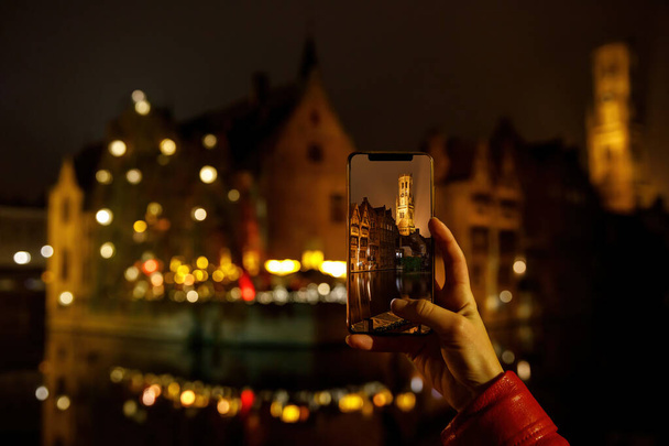 Belçika 'nın eski Brugge kasabasının fotoğrafını çekmek gece aydınlandı. Akıllı telefonlu turist - Fotoğraf, Görsel
