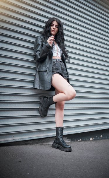 Νεαρή γυναίκα κάπνισμα, μόδα και streetwear με genz punk στυλ, υπαίθρια και μοντέρνα, νευρικός στην αστική πόλη. Νεολαία, εστίαση και ομορφιά με ροκ αισθητική, μοντέλο μόδας σε ρούχα σχεδιαστών στο Λονδίνο. - Φωτογραφία, εικόνα