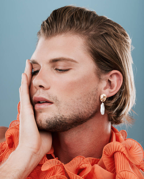 LGBTQ, fashion and face of queer man with orange clothes, accessories and facial cosmetics on blue background. Transgender, gay or non binary model with beauty makeup, skincare glow or creative style. - Fotoğraf, Görsel