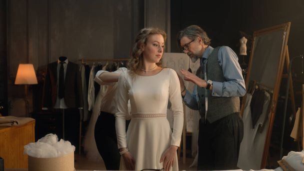 Cinematic shot of tailors taking measurements of woman for wedding dress. Bride on fitting wedding dress in luxury designer atelier or tailoring studio. Concept of fashion, handmade and couturier. - Foto, Bild