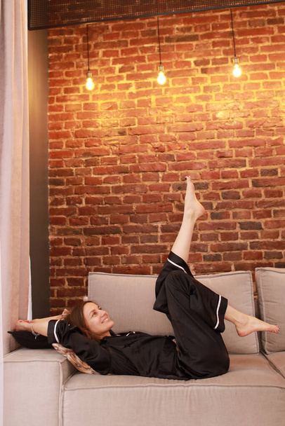 Kick back and relax concept. Happy woman on comfortable soft sofa enjoying stress free weekend or vacation at home, calm satisfied girl stretching on couch thinking of pleasant lazy day, dreaming. - Photo, image