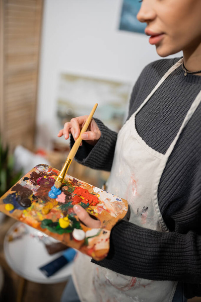 Cropped view of artist in apron mixing paints on palette in workshop  - Fotó, kép