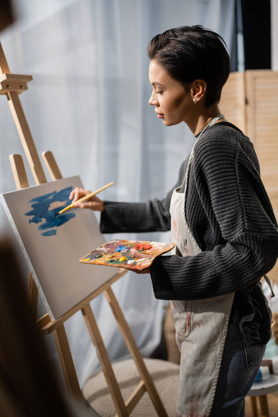 Side view of brunette artist painting on canvas in studio  - Foto, imagen