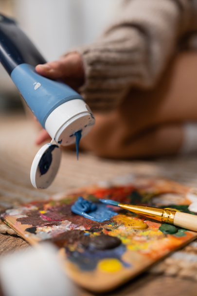 Cropped view of artist pouring paint on palette near paintbrush in workshop  - Fotó, kép