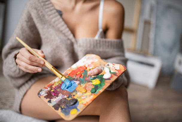Cropped view of burred artist holding paintbrush and palette in workshop  - Fotoğraf, Görsel