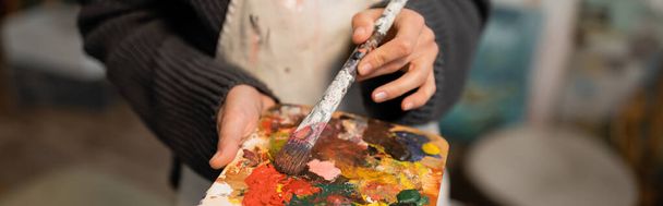 Cropped view of woman in apron holding palette and paintbrush, banner  - Foto, Bild