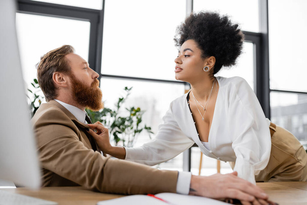 curly african american woman adjusting jacket of bearded man in office  - Photo, image
