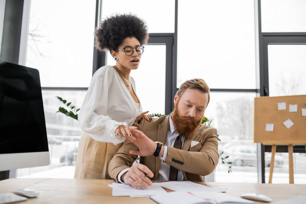 curly african american woman trying to seduce tensed businessman working with documents  - Foto, Bild