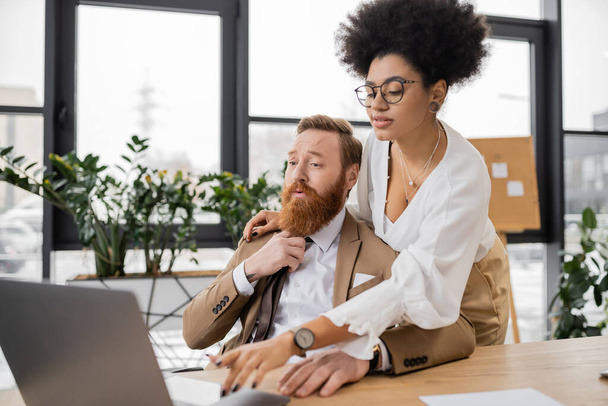 curly african american woman using laptop near bearded businessman pulling tie in office  - Foto, immagini