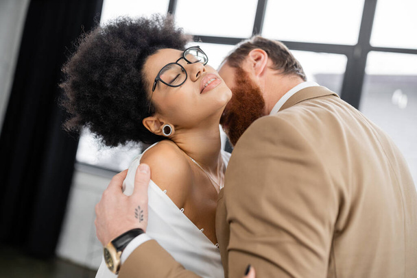 tattooed man undressing and kissing neck of seductive african american woman in office  - Fotografie, Obrázek
