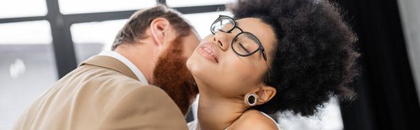 bearded man kissing neck of seductive african american woman with closed eyes, banner  - Zdjęcie, obraz