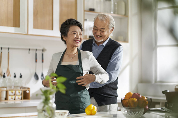 люблячий старший азіатський чоловік допомагає дружині зав'язувати фартух на кухні вдома
 - Фото, зображення
