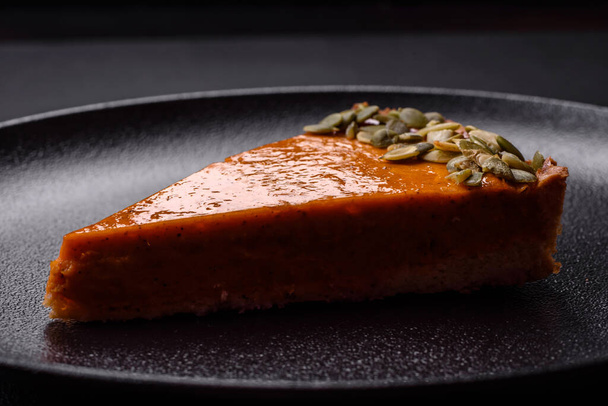Beautiful tasty pumpkin pie with slices on a black ceramic plate on a dark concrete background - Foto, afbeelding