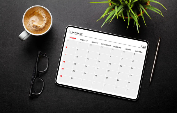 Tablet con app calendario, tazza di caffè e forniture per ufficio sulla scrivania. Vista dall'alto piatto lay - Foto, immagini