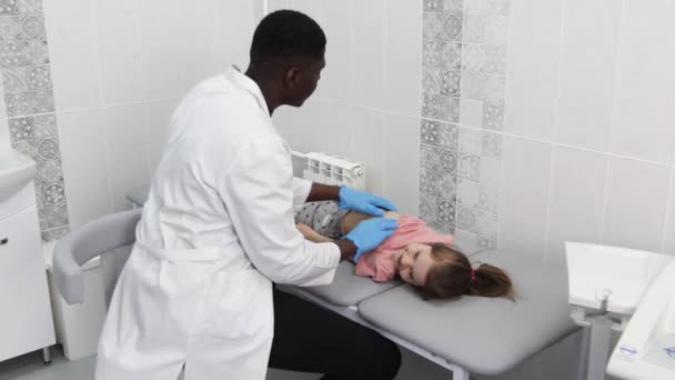 Ένα κοριτσάκι σε ένα παιδιατρικό τσεκάπ με το γιατρό της. Ένας Αφροαμερικανός γιατρός εξετάζει τα εσωτερικά όργανα της κοιλιακής κοιλότητας ενός παιδιού. - Πλάνα, βίντεο